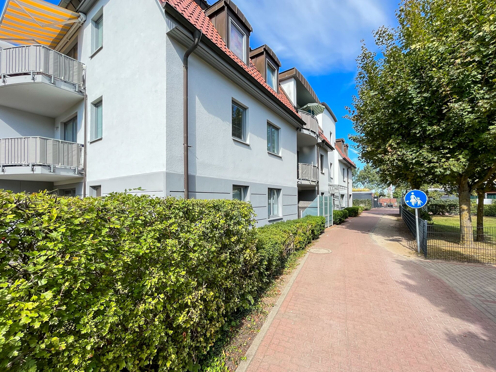 A residential building with balconies, a paved walkway, and a blue pedestrian sign.
