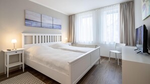 A modern hotel room with a large bed, bedside tables, a desk, and a television. - Sünnslag Wohnung 127 (Ostseebad Boltenhagen)