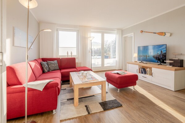 Ett modernt vardagsrum med en röd soffa, ett träbord och en tv som står på ett vitt skåp.