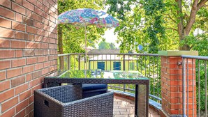 En balkon med fletningsmøbler, et glasbord og en farverig parasol.