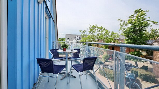 A balcony with blue walls, a table with chairs, and a view of the street and buildings.