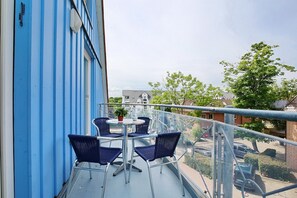 Un balcon aux murs bleus, une table avec des chaises et une vue sur la rue et les immeubles.