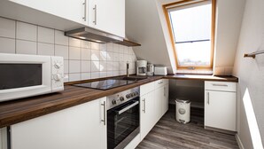 A compact kitchen with white cabinets, a microwave, a stove, and a window above the sink.