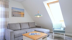 A modern living room with a grey sofa, a wooden coffee table, a blue pendant light, and a view of the sea through a window.