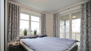 Un dormitorio moderno con una cama grande, mesitas de noche, una ventana con cortinas y vistas al exterior.
