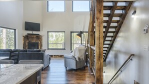 Un vaste espace de vie doté d’un plancher en bois, d’un canapé, d’une télévision et d’un escalier.
