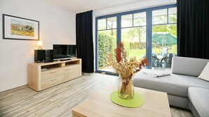 Ein modernes Wohnzimmer mit einem Holz-TV-Möbel, einem grauen Sofa, einem grünen Tisch mit einer Vase und einem großen Fenster mit Vorhängen.