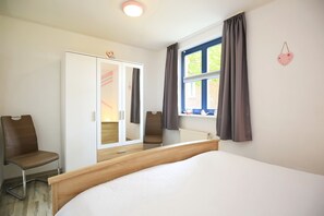Ein Schlafzimmer mit Bett, Kleiderschrank, Stuhl und einem Fenster mit Vorhängen.