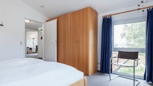 A bedroom with a bed, a wooden wardrobe, and a window with curtains. - Die Ferienwohnung 21 in der Anlage Godewind ist Eine 3-zimmerwohnung für bis zu (Ostseebad Boltenhagen)