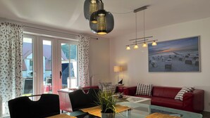 A modern living room with a glass coffee table, red leather sofa, and a large painting of a beach scene. - Strandvilla Niklot Wohnung 01 (Ostseebad Boltenhagen)