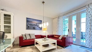 A living room with a red sofa set, a glass coffee table, a painting on the wall, and a view through the sliding glass door.