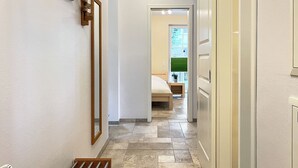 A hallway with a wooden slat ceiling, a bed with a green window, and a bathroom visible through an open door.