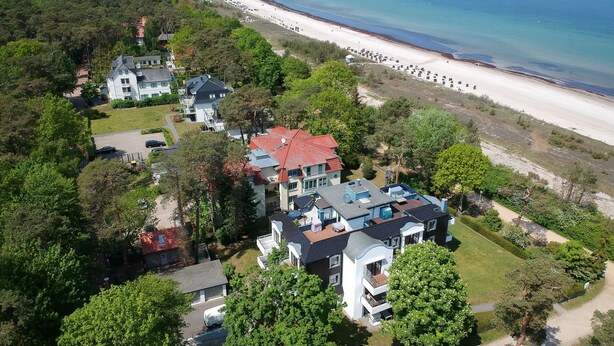 An aerial view of a coastal residential area with houses, a beach, and a pier.