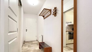 A hallway with a white door, a wooden bench, a radiator, and a mirror reflecting a kitchen area.