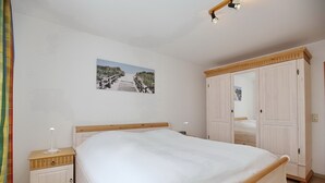 Ein Schlafzimmer mit einem großen Bett, einem Nachttisch, einem Kleiderschrank und einem Bild an der Wand.