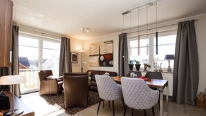 A modern living room with a sofa, two armchairs, a dining table, and a large window with curtains. - Villa Bernstein Wohnung 06 (Ostseebad Boltenhagen)