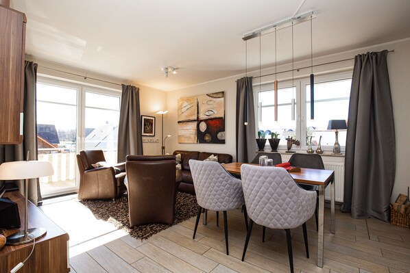 A modern living room with a sofa, two armchairs, a dining table, and a large window with curtains. - Villa Bernstein Wohnung 06 (Ostseebad Boltenhagen)