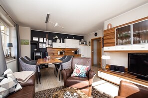 Ein modernes Wohnzimmer mit einer Couch, Sesseln, einem Couchtisch und einem Fernseher.