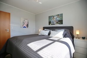 A neatly made bed with a quilted cover, a headboard, and two bedside lamps. - Villa Bernstein Wohnung 06 (Ostseebad Boltenhagen)