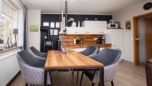 A modern kitchen with a wooden table and four chairs, a black and white color scheme, and a view of the outdoors. - Villa Bernstein Wohnung 06 (Ostseebad Boltenhagen)