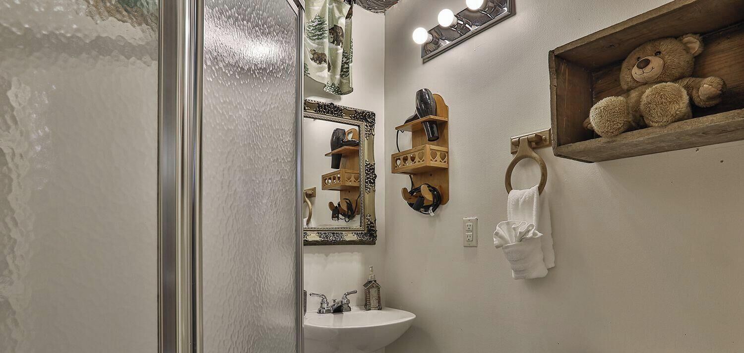 Un bany amb un lavabo de pedestal, un vàter, un mirall amb il·luminació, un porta tovalloles i una prestatgeria amb un os de peluix.