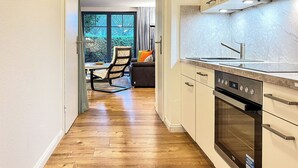 Una cocina moderna con horno empotrado, un comedor con mesa y sillas, y vistas al verdor a través de amplias ventanas.