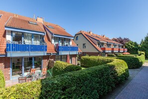 Uma fileira de edifícios residenciais modernos com varandas, um caminho pavimentado e sebes bem cuidadas.