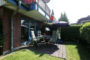 Um pátio com mesa e cadeiras, um deck de madeira e uma porta de vidro que dá para um quarto.
