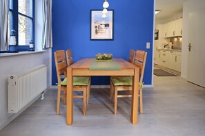 Uma área de refeições com uma mesa e cadeiras de madeira, um quadro na parede e uma janela com cortinas.