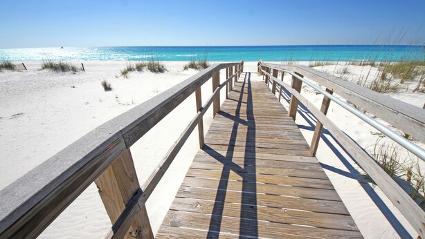 Une promenade en bois qui mène à une plage aux eaux d’un bleu limpide.