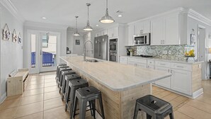 Une cuisine moderne avec des meubles blancs, un grand îlot central doté de tabourets, des appareils en acier inoxydable et un éclairage suspendu.