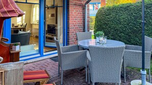 Une terrasse extérieure avec des meubles en osier, une table et un parasol rouge.