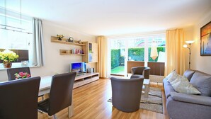 Un salon moderne comprenant un canapé, des fauteuils, un téléviseur et un coin repas avec une table et des chaises.