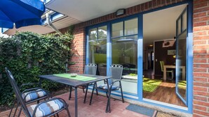 Een terras buiten met een tafel, stoelen, een blauwe parasol en een bakstenen muur.