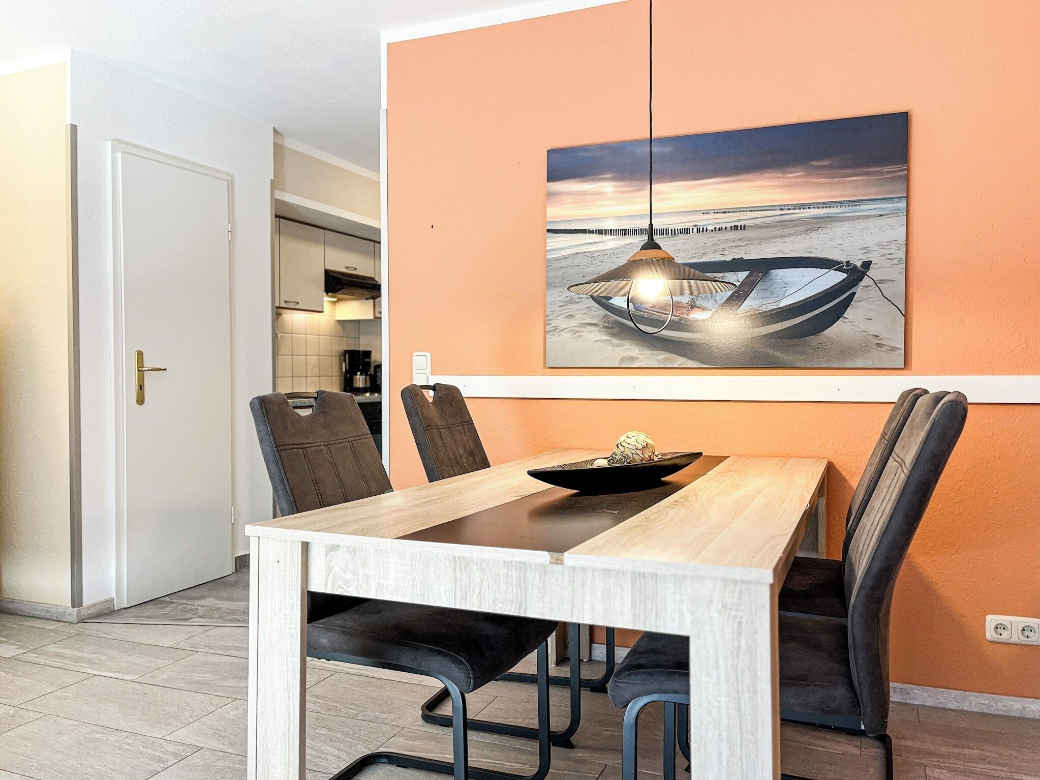 A dining area with a wooden table, black chairs, and a wall-mounted painting of a boat on a beach.