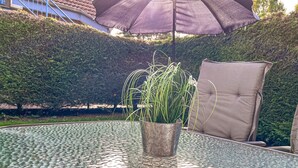 A glass-top table with a metal planter containing green plants, a brown cushioned chair, and a large purple umbrella.