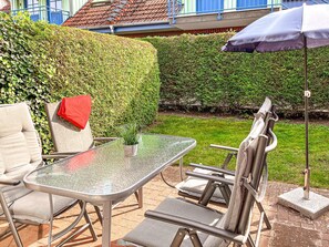 Eine Terrasse im Freien mit einem Glastisch, Metallstühlen und einem blauen Sonnenschirm.