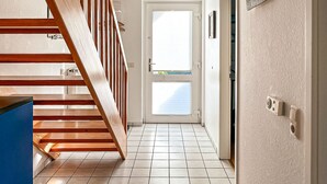 Un couloir avec un escalier en bois, une porte dotée d’une fenêtre et un luminaire fixé au mur.