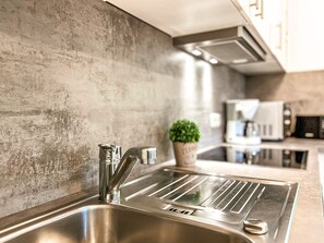 A modern kitchen with a stainless steel sink, a potted plant, and a coffee machine. - Urlauberdorf Haus 53a (Ostseebad Boltenhagen)