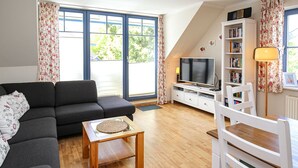A living room with a sofa, a coffee table, a TV, a bookshelf, and a lamp. - Papillon Wohnung 10-8 (Ostseebad Boltenhagen)