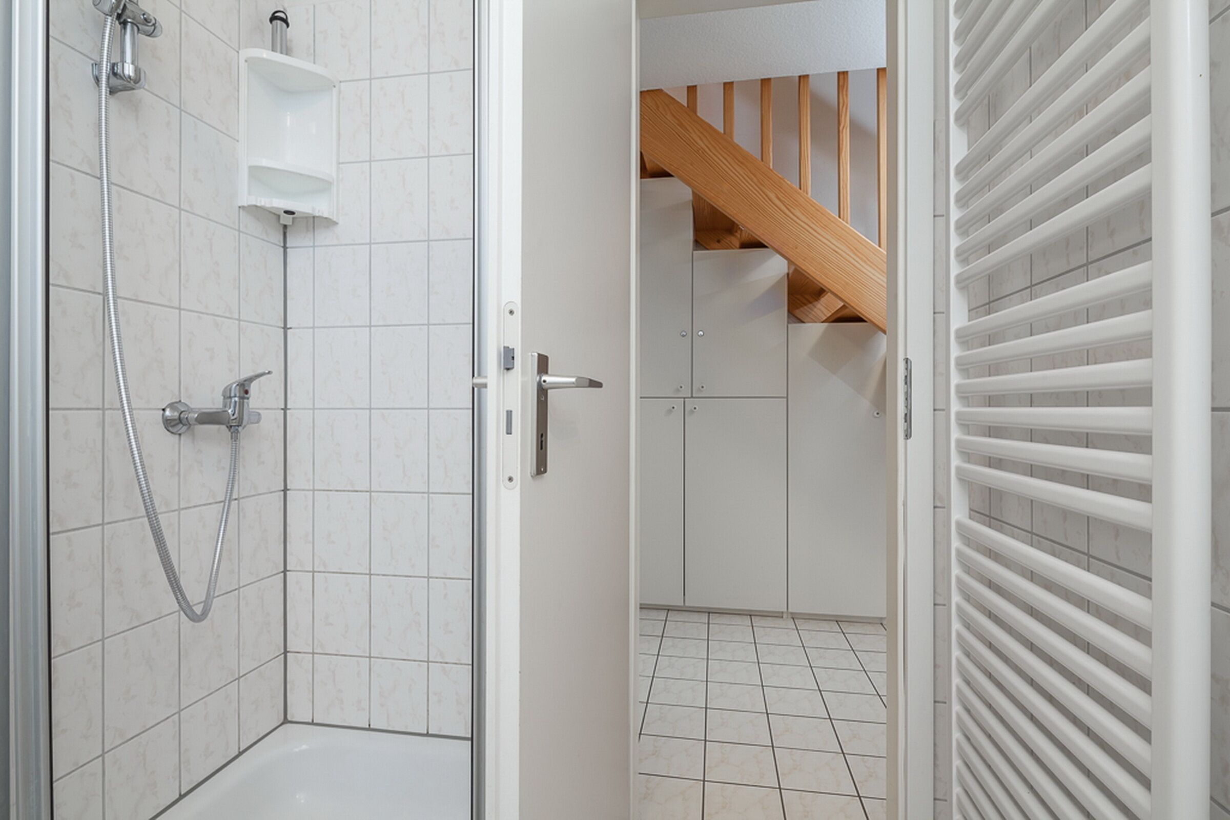 A bathroom with a shower, a toilet, and a sink. There is a wooden staircase in the background.
