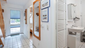 Ein Hotelzimmer mit einer Holztreppe, einer Tür zu einem Balkon, einem weiß gefliesten Boden, einem großen Spiegel und einem Badezimmer mit Waschbecken und Handtuchhalter.