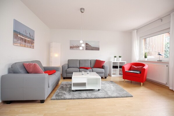 Ein modernes Wohnzimmer mit grauem Sofa, einem roten Sessel, einem weißen Couchtisch und Kunstwerken an den Wänden.