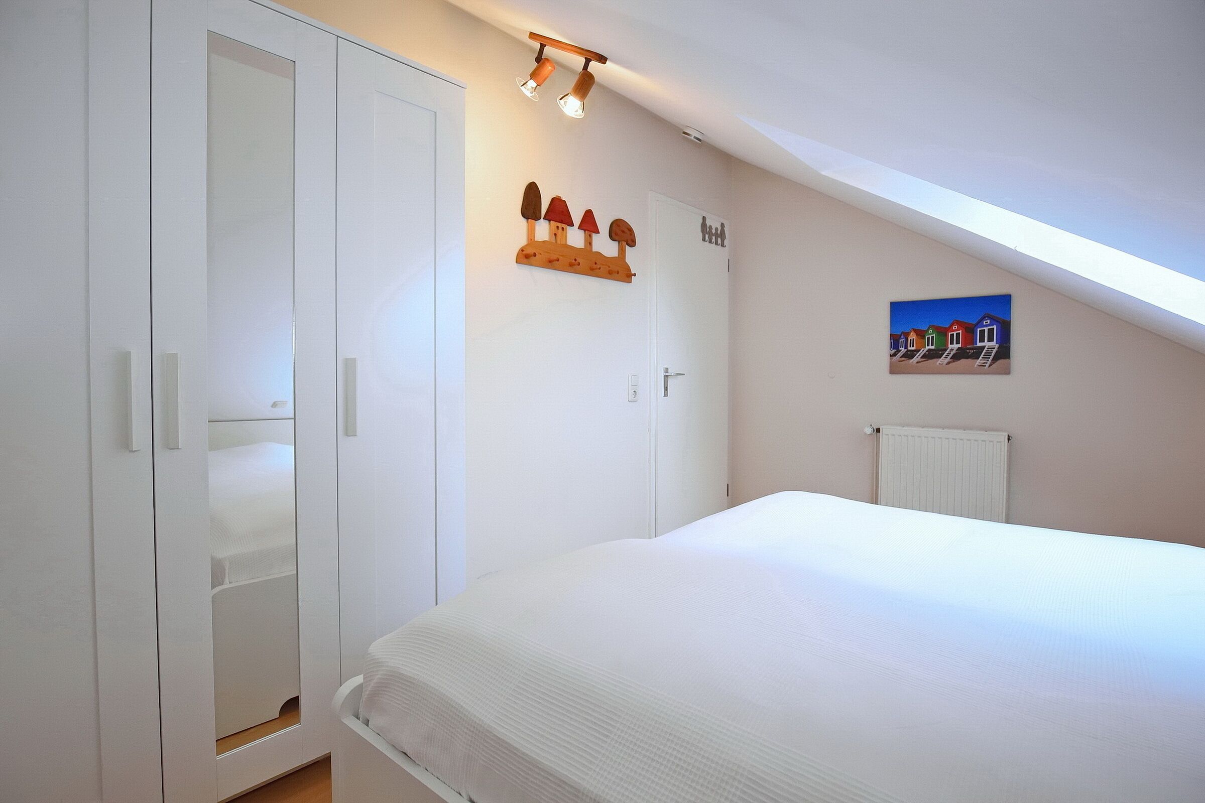A bedroom with a large bed, a wardrobe, a radiator, and a painting on the wall.