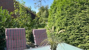 A table with a woven placemat and a potted plant, two checkered chairs, and a hedge in the background. - Urlauberdorf Wohnung 21b (Ostseebad Boltenhagen)
