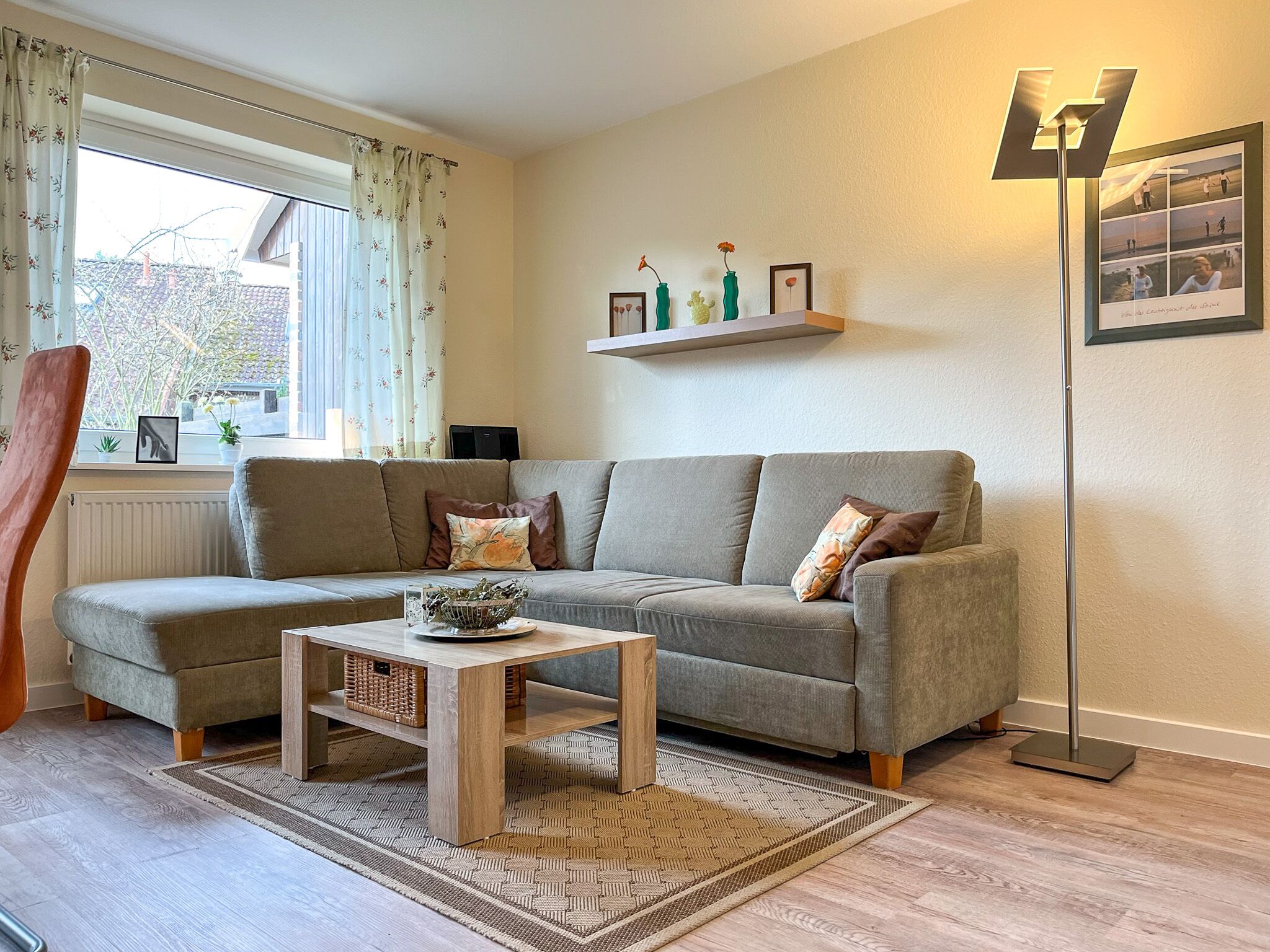 Un salon avec un canapé gris, une table basse en bois, un lampadaire et une étagère ornée d’objets décoratifs.