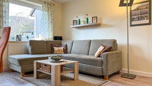 Ein Wohnzimmer mit grauem Sofa, einem Holztisch, einer Stehlampe und einem Regal mit Dekoration.