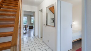 Ein modernes Interieur mit einer Holztreppe, einem Flur, der zu einem Zimmer mit einem Bett führt, und einer Tür mit einem Spiegel.