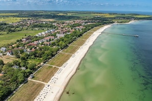 An aerial view of a coastal town with a long sandy beach, a pier extending into the water, and a mix of residential and commercial buildings.