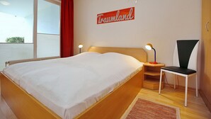 Habitación de hotel con una cama grande, una mesita de noche con lámpara, una silla y una ventana con vistas.